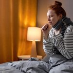 Kaszląca kobieta, która siedzi w łóżku w szaliku