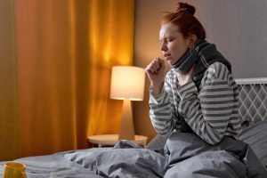 Kaszląca kobieta, która siedzi w łóżku w szaliku